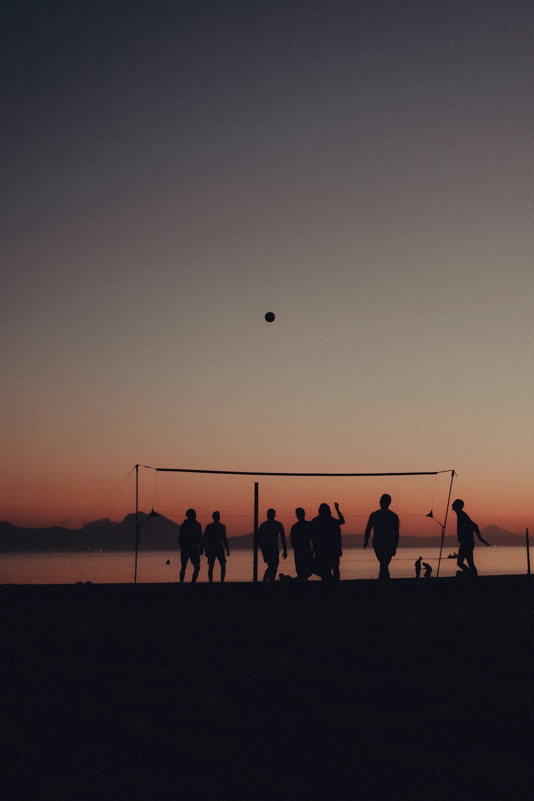 People play volleyball on a sandy beach at sunset.